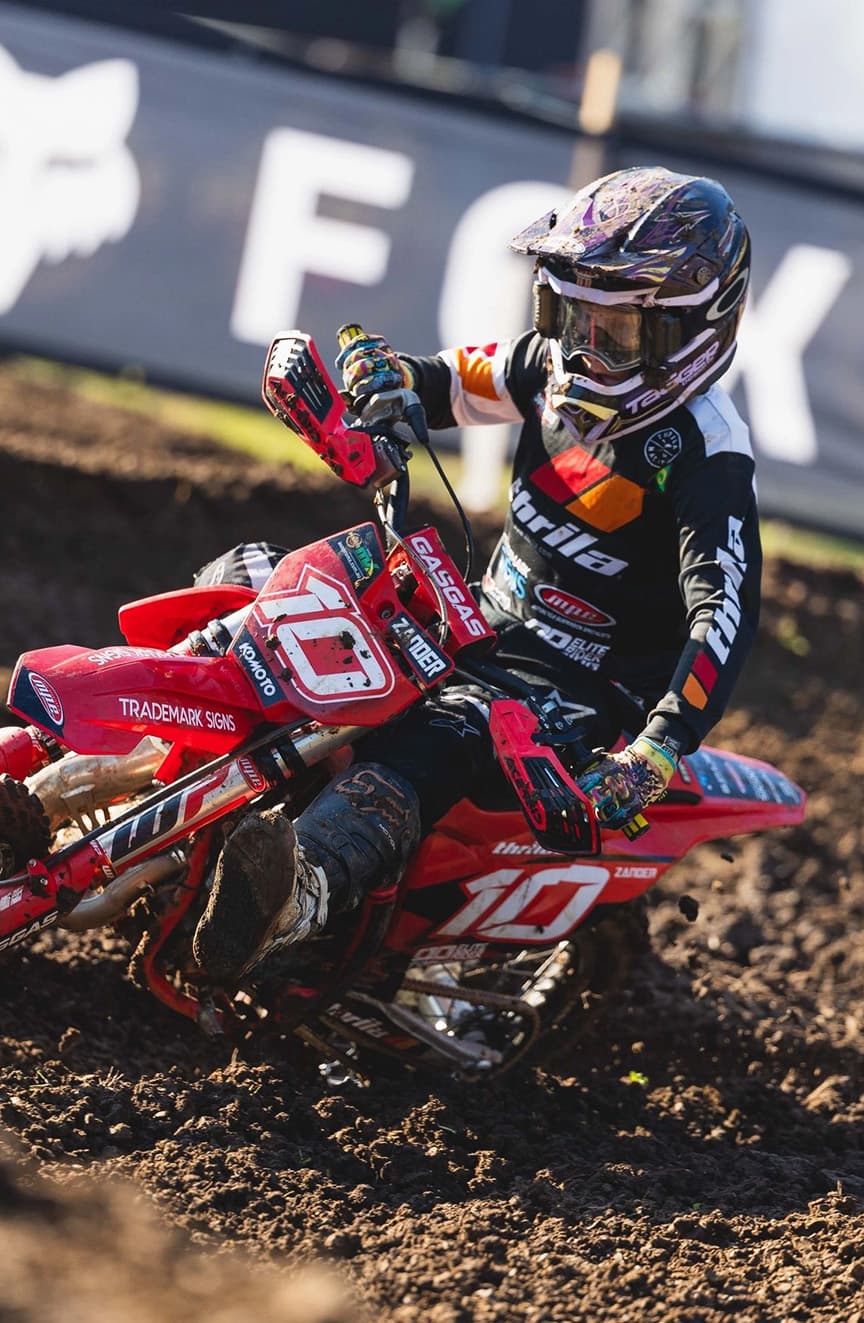 A young MX85 rider on a red motorcycle on a dirt track