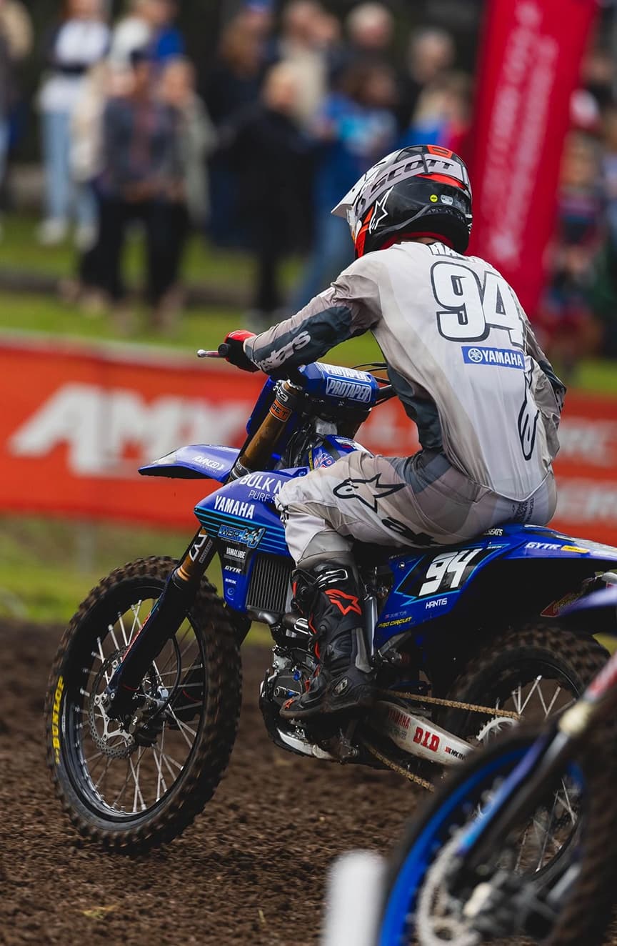 An MX3 rider on a blue motorbike on a dirt track