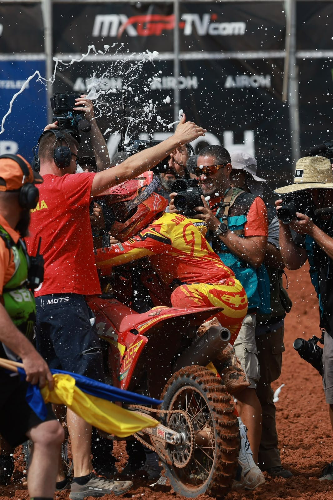 Motocross rider celebrates among team members and photographers as liquid sprays through the air after racing at MXGP Australia.