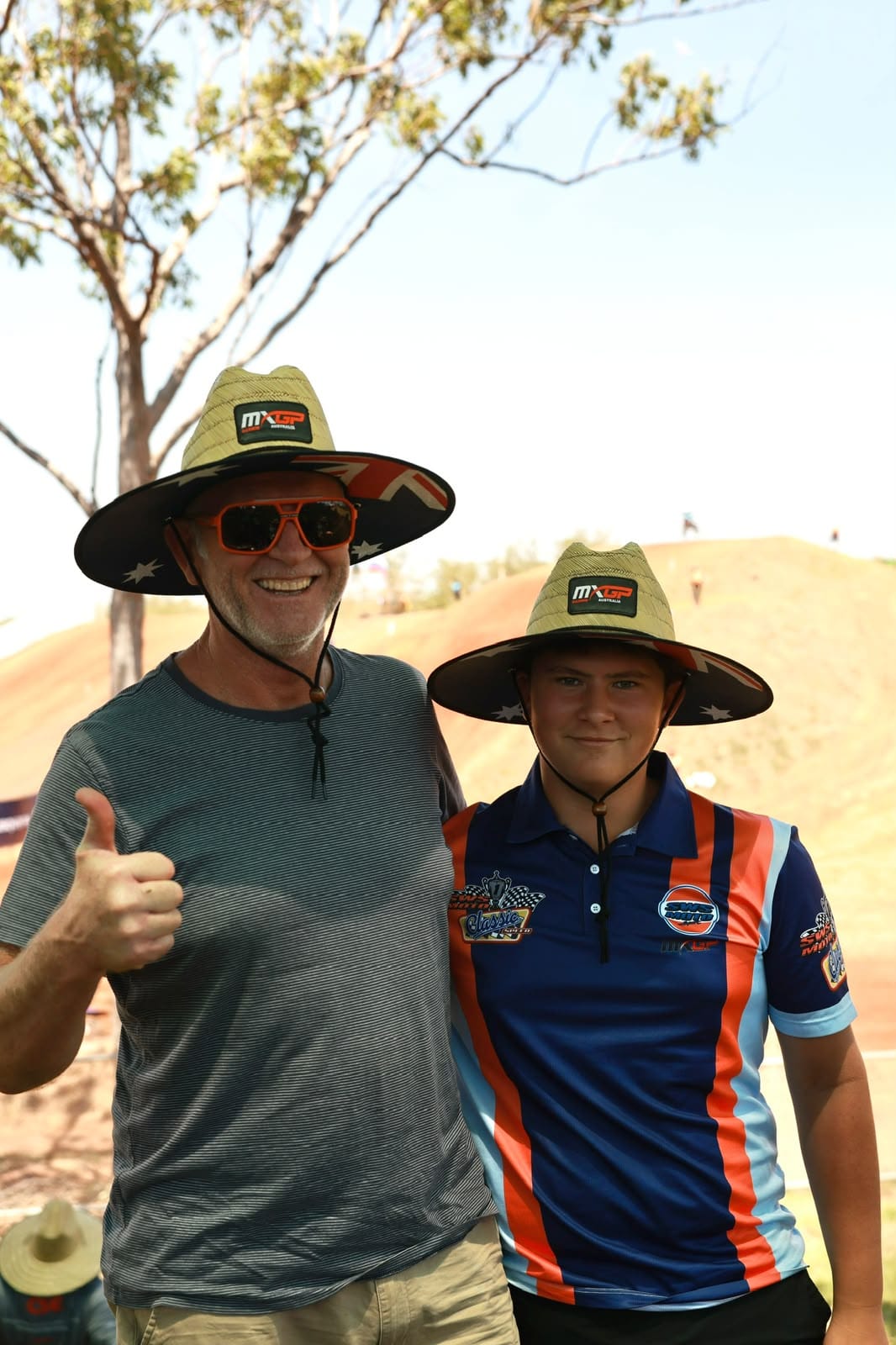 An adult and young spectator wearing MXGP of Australia hats pose beside the motocross track at Hidden Valley.