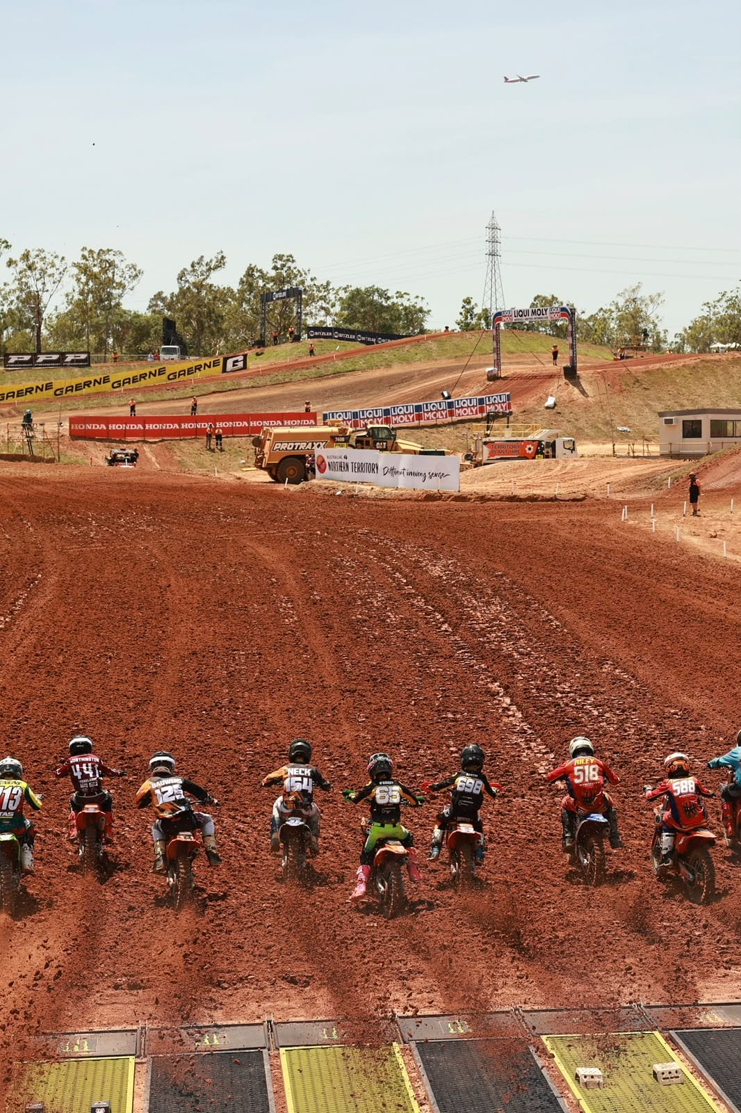Motocross riders launch from the start gates and race up the red dirt track at MXGP of Australia.