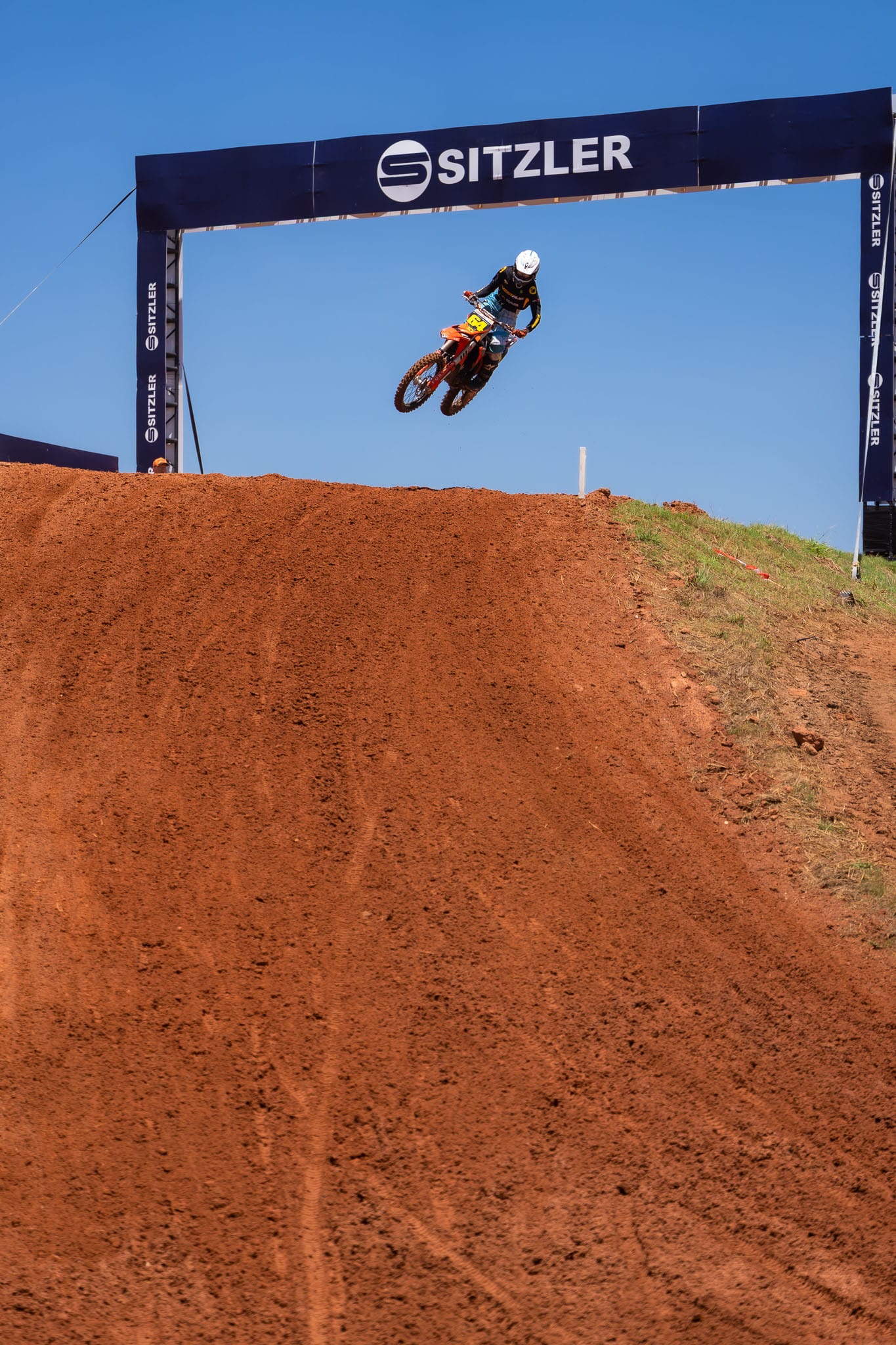 Motocross rider jumps beneath the Sitzler track structure against a clear blue sky at MXGP of Australia.