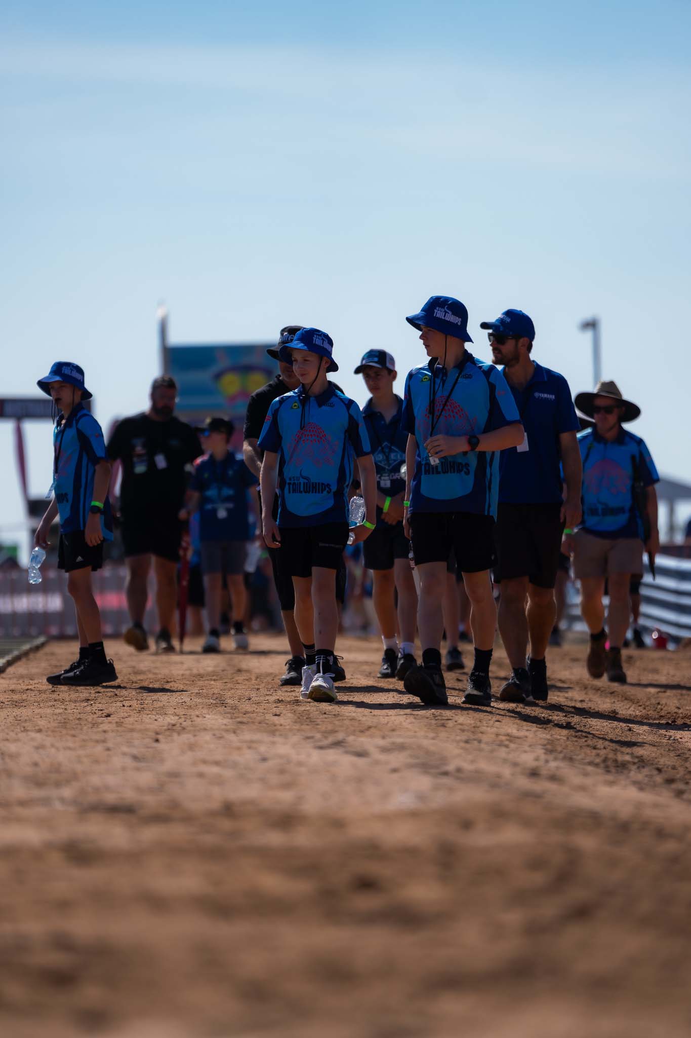 Young MXGP of Australia attendees in matching blue shirts and hats walking through the Hidden Valley event precinct.