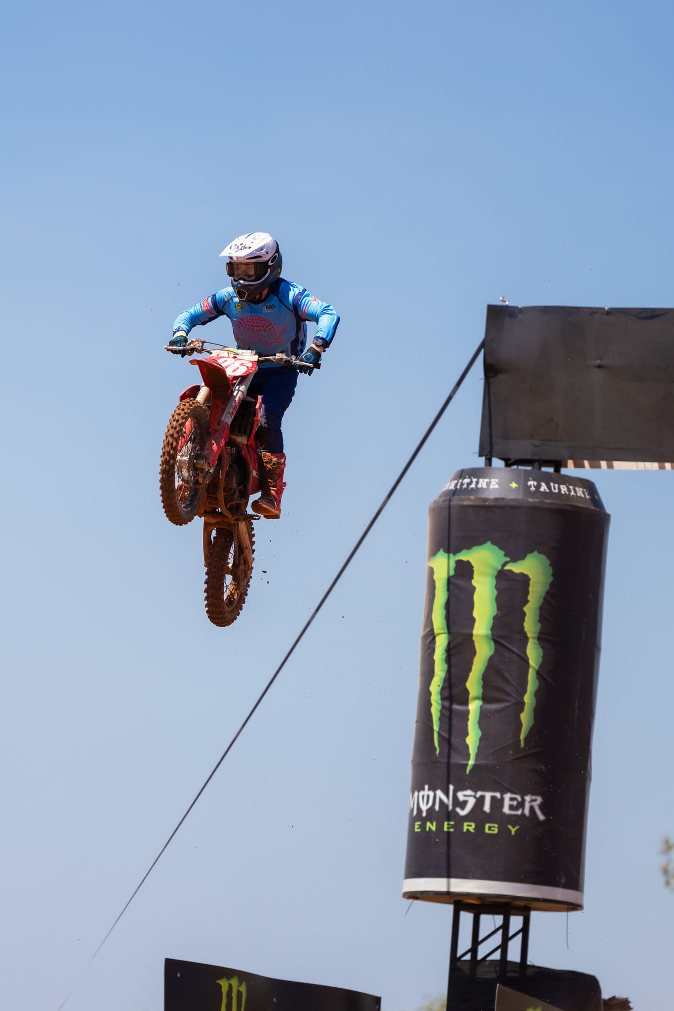 Motocross rider jumps beside a Monster Energy track structure against the blue sky at MXGP of Australia.