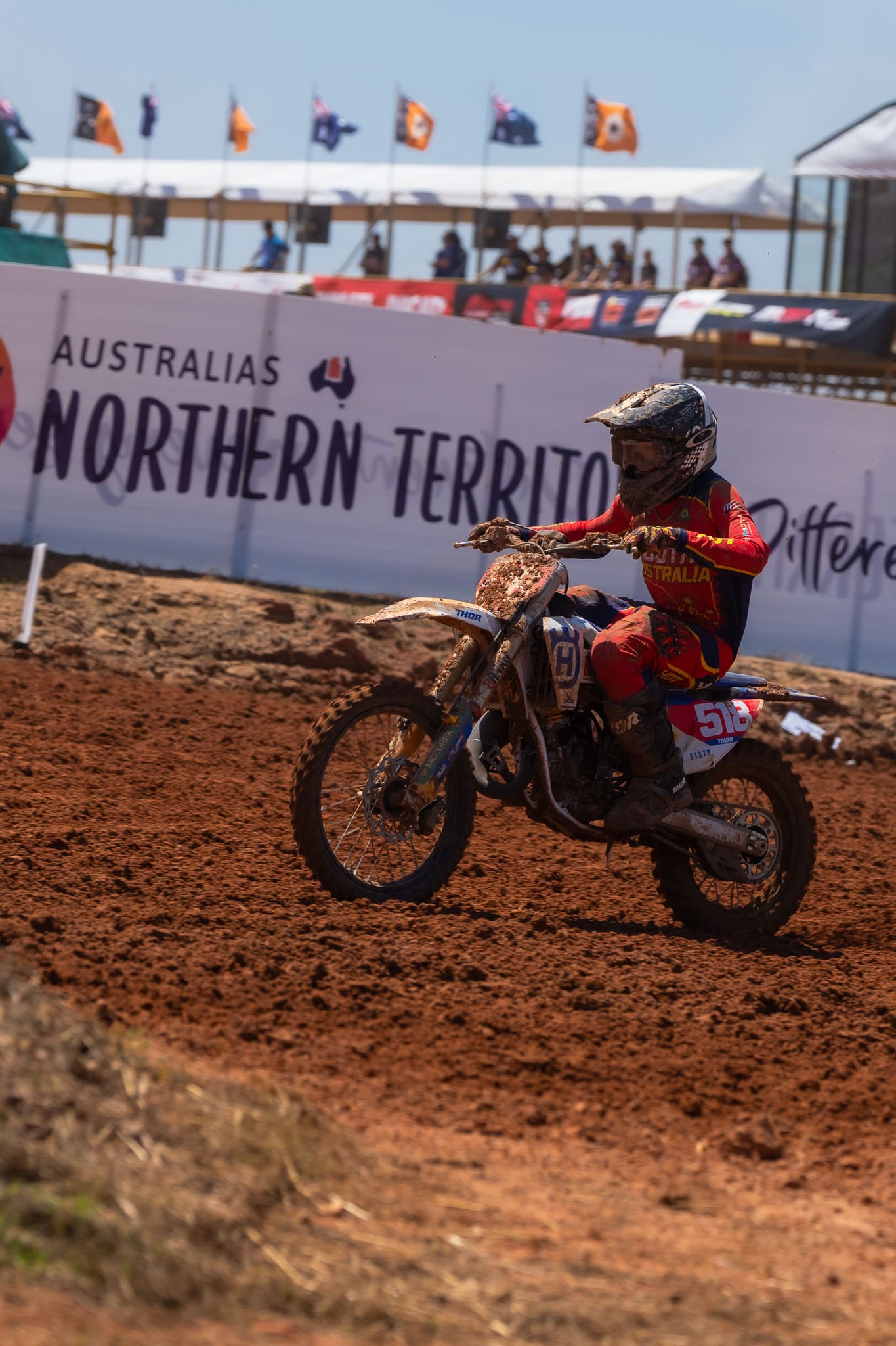 Mud-covered South Australia motocross rider number 518 races along the red dirt track at MXGP of Australia.