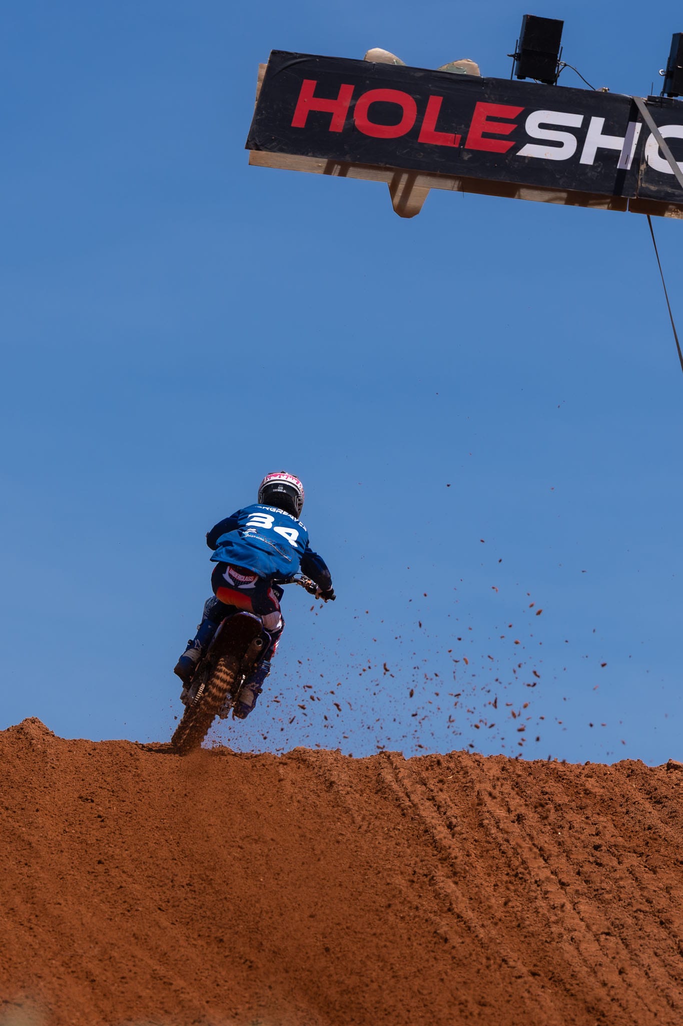 Motocross rider accelerates over a red dirt rise beneath the Holeshot structure at MXGP of Australia in Darwin.