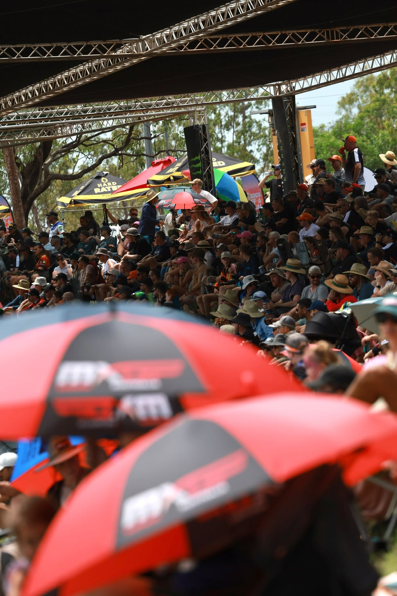 Large crowd watches the action from a shaded grandstand, with MXGP Australia umbrellas visible in the foreground.