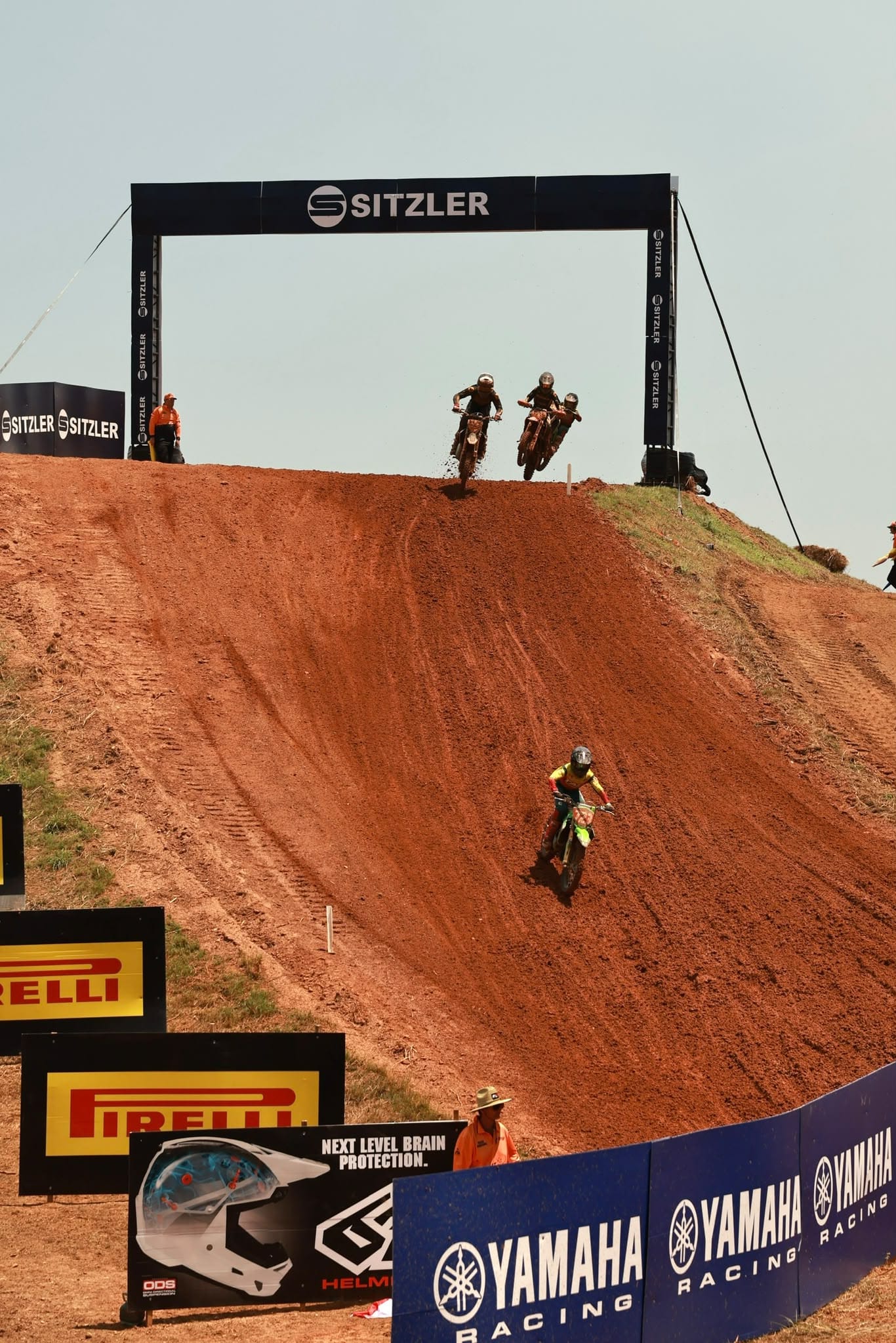 Motocross riders descend a steep red dirt hill beneath the Sitzler track structure at MXGP of Australia.