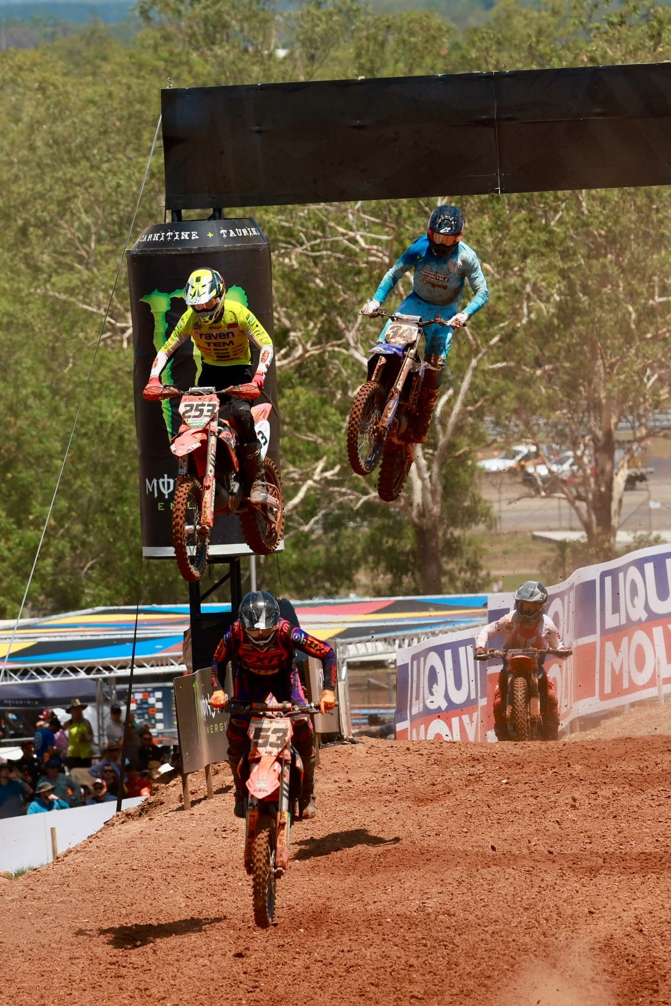 Several motocross riders jump and race over a crest beneath the finish structure during MXGP Australia in Darwin.