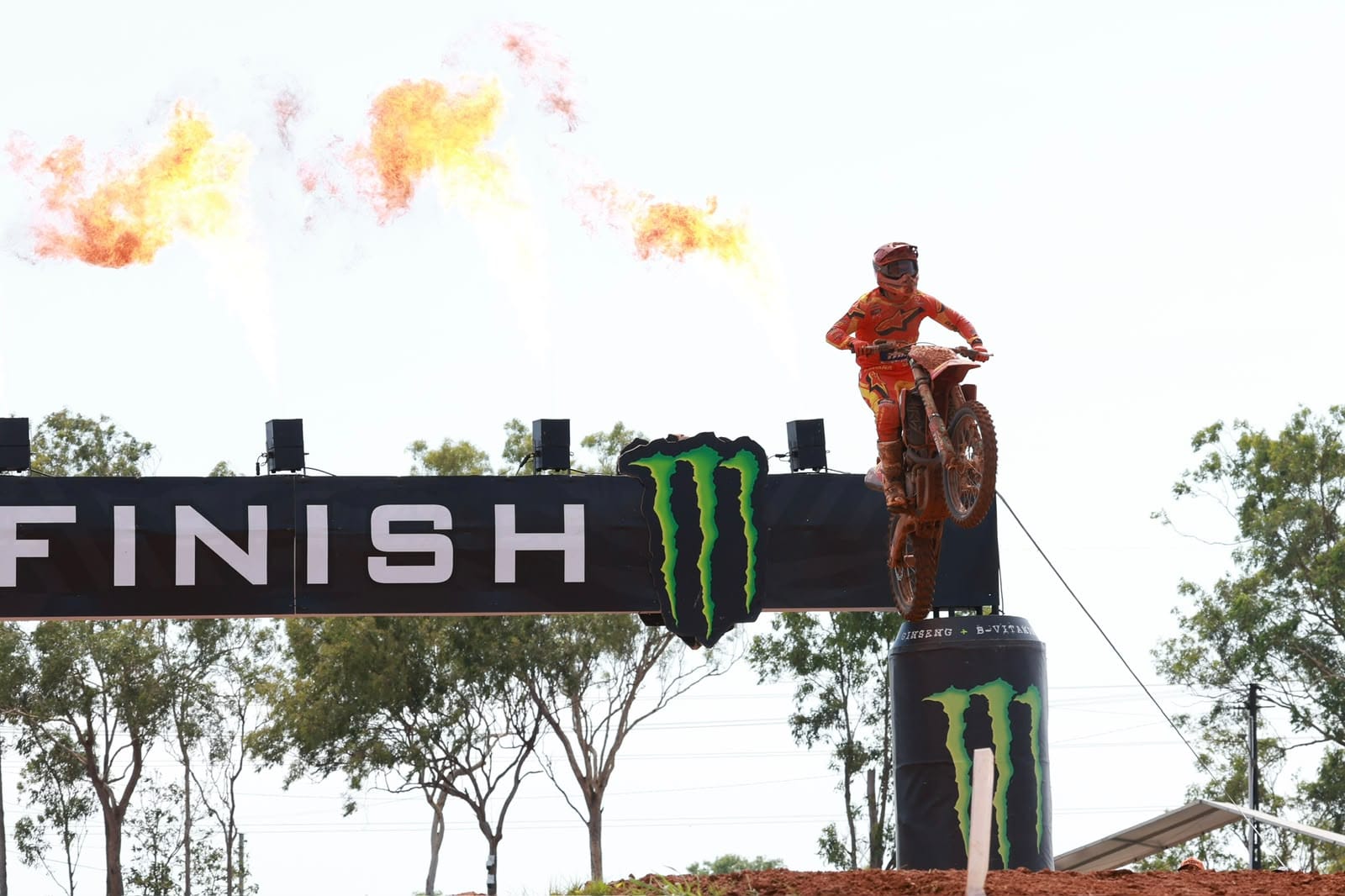 Motocross rider jumps past the MXGP finish line as flames burst above the track during racing in Darwin.