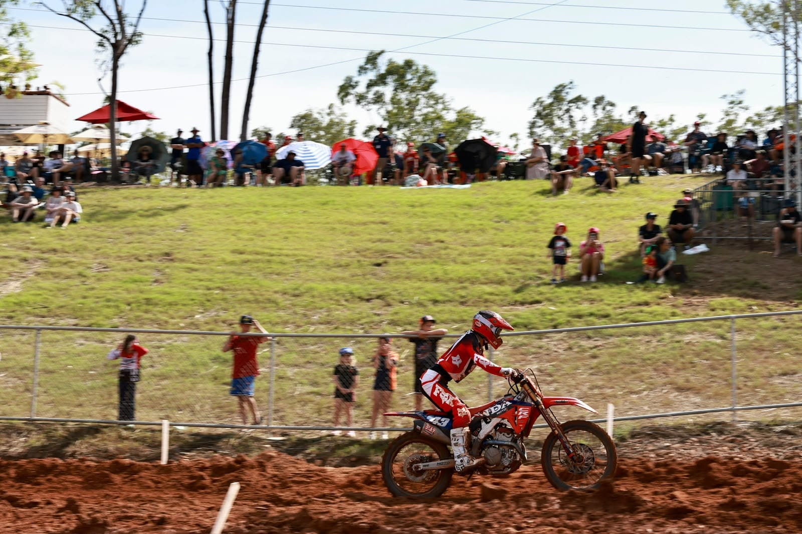 Motocross rider races along the track in front of spectators gathered on a grassy hillside at MXGP Australia.