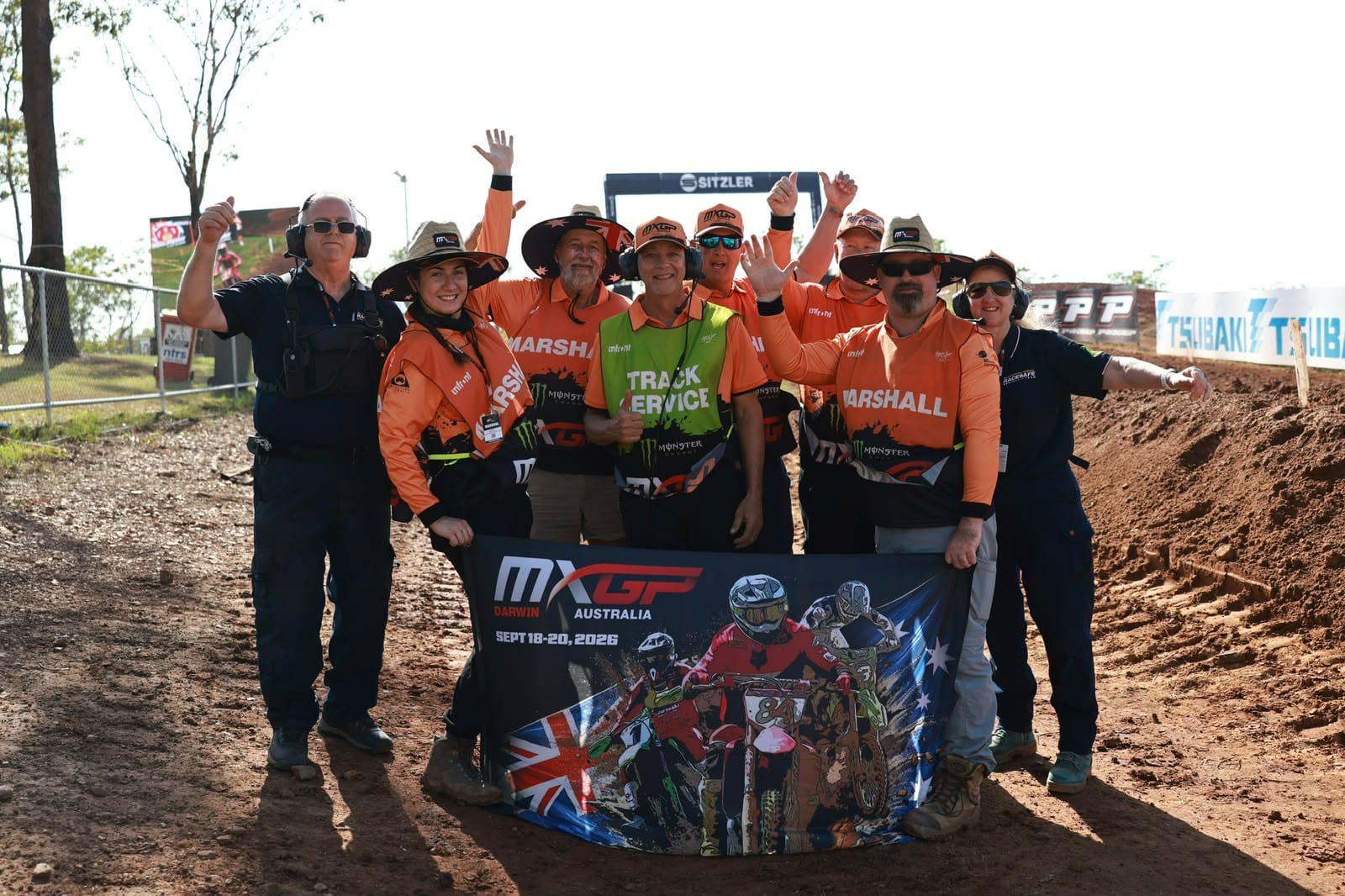 MXGP Australia event officials and track staff pose together beside the motocross track holding an MXGP Darwin 2026 banner.