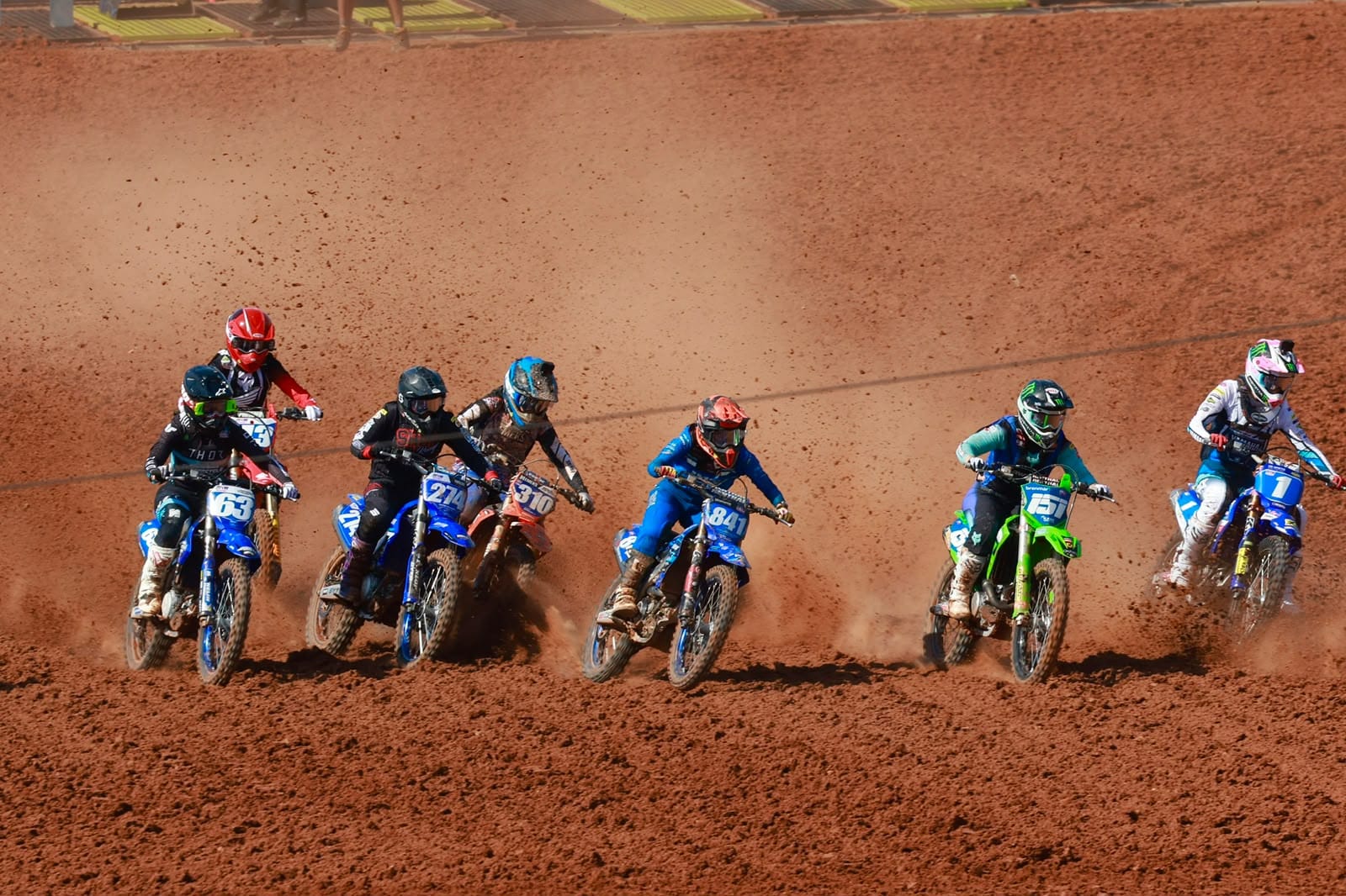 Group of motocross riders race through a sweeping red dirt corner, kicking up dust during MXGP Australia in Darwin.