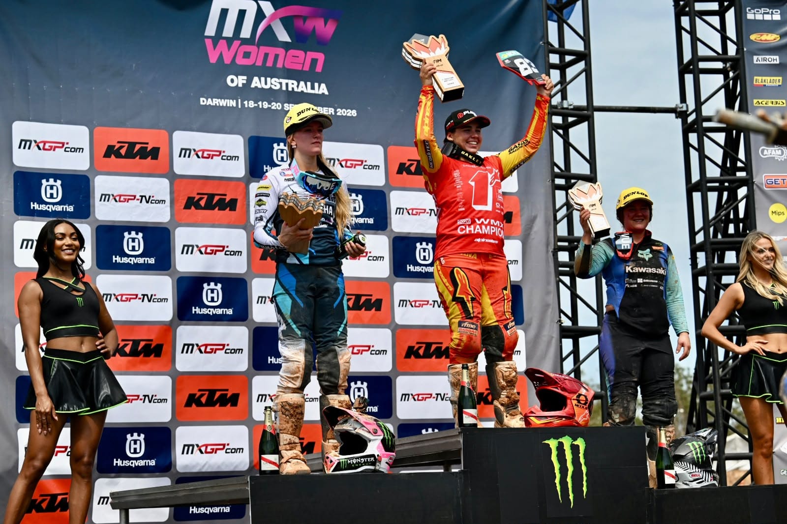 Women’s motocross champion celebrates on the podium with her trophy raised, flanked by the second- and third-place riders at MXGP Australia in Darwin.