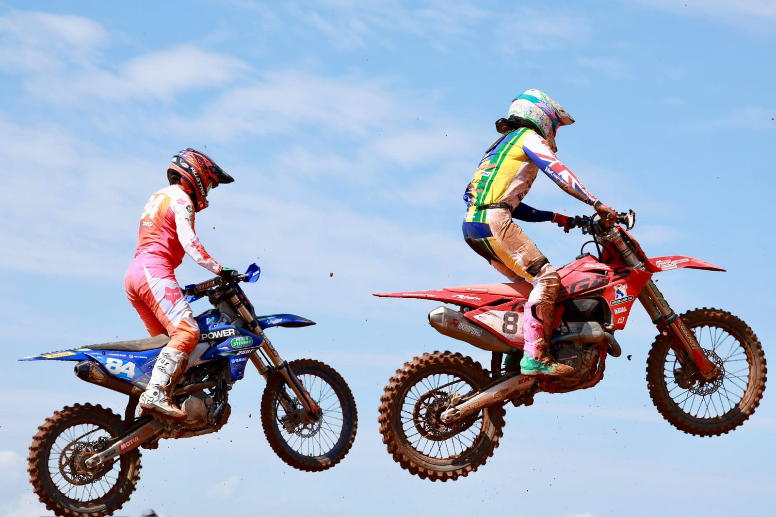 Two motocross riders jump side by side against a blue sky during racing at MXGP Australia in Darwin.